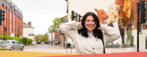 Young woman stood outside in Hereford. Artwork of a cow and it's calf is visible in the background. 